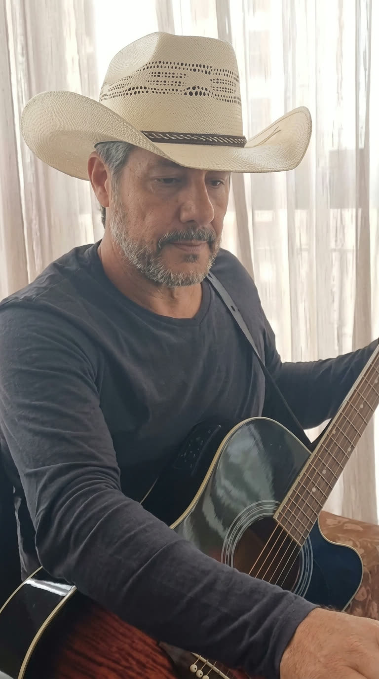 Gleno Rossi de chapéu de palha tocando violão em casa